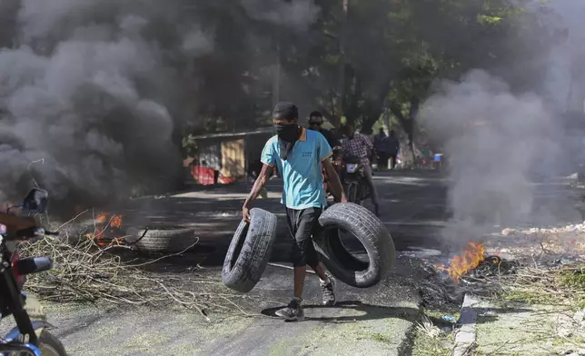 A resident carries tires to be added to a burning barricade to deter gang members from entering his neighborhood, in Port-au-Prince, Haiti, Tuesday, Nov. 19, 2024. (AP Photo/Odelyn Joseph)