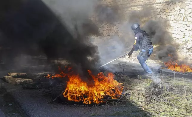 A police officer works to clear barricades of burning tires set on fire by residents to deter gang members from entering their neighborhood, in Port-au-Prince, Haiti, Tuesday, Nov. 19, 2024. (AP Photo/Odelyn Joseph)