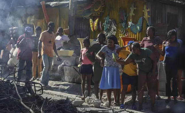 A woman films a scene where the bodies of suspected gang members who were set on fire by residents sit in a heap in the middle of a road, in the Pétion-Ville neighborhood of Port-au-Prince, Haiti, Tuesday, Nov. 19, 2024. (AP Photo/Odelyn Joseph)