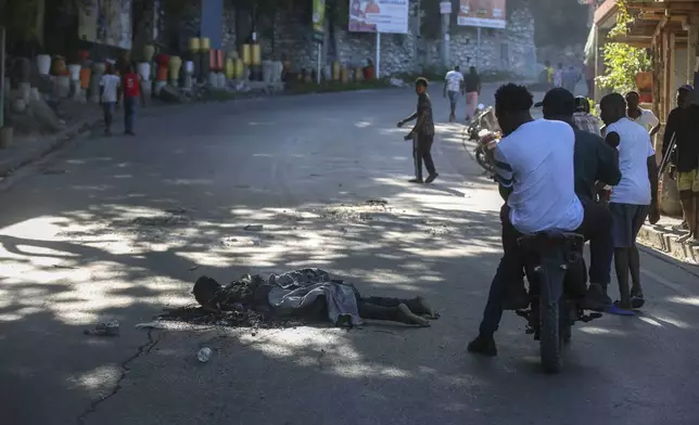 Passersby look at the abandoned body of an alleged gang member who was set on fire by residents, in the Pétion-Ville neighborhood of Port-au-Prince, Haiti, Tuesday, Nov. 19, 2024. (AP Photo/Odelyn Joseph)