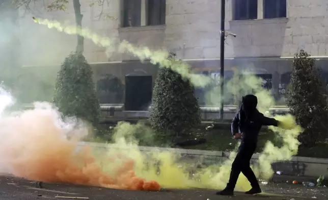 A demonstrator throws a firecracker toward police as police block a street to prevent protesters rallying against the government's decision to suspend negotiations on joining the European Union for four years, outside the parliament's building in Tbilisi, Georgia, early Saturday, Nov. 30, 2024. (AP Photo/Zurab Tsertsvadze)