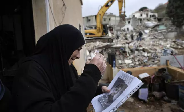 A woman mourns holding a portrait of her grandson, a Hezbollah fighter who was killed in the fighting with Israeli troops, as she waits for rescuers to recover his body from under the rubble of a destroyed house, background, in Ainata village, south Lebanon, following a ceasefire between Israel and Hezbollah on Wednesday, Nov. 27, 2024. (AP Photo/Hussein Malla)