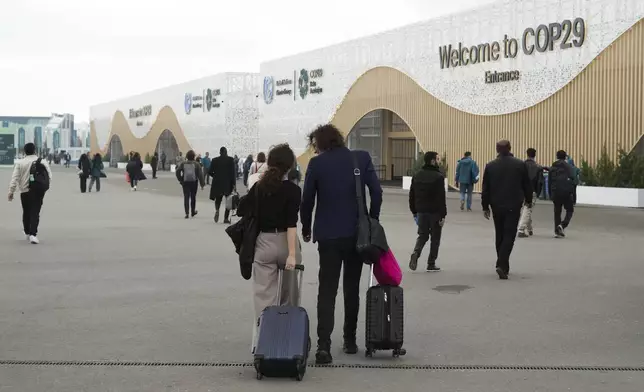 Attendees pull luggage as they walk into the venue for the COP29 U.N. Climate Summit, Saturday, Nov. 23, 2024, in Baku, Azerbaijan. (AP Photo/Sergei Grits)