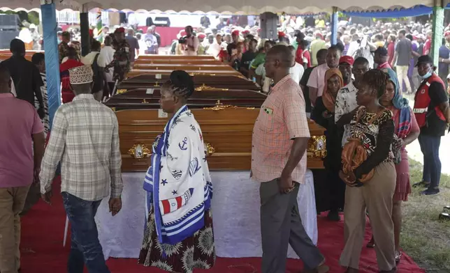 People walk past coffins in Dar es Salaam, Tanzania Monday, Nov. 18, 2024 during a funeral ceremony for the people who died in a building that collapsed in Dar es Salaam on Saturday. (AP Photo)