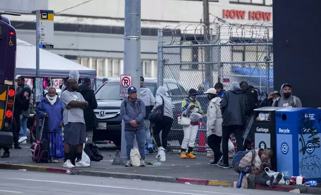 People wait for a bus near the area where multiple people were stabbed earlier Friday, Nov. 8, 2024, in the Chinatown-International District in Seattle. (AP Photo/Lindsey Wasson)