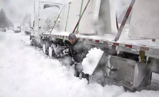 Truck driver Kirill Foken shovels a trench alongside his truck's tires to free it up as he awaits for I-5 to reopen in Weed, Calif., Wednesday, Nov. 20, 2024. (Carlos Avila Gonzalez/San Francisco Chronicle via AP)