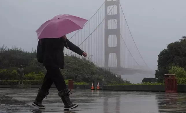 A pedestrian carrying an umbrella walks in front of the Golden Gate Bridge in San Francisco, Wednesday, Nov. 20, 2024. (AP Photo/Jeff Chiu)