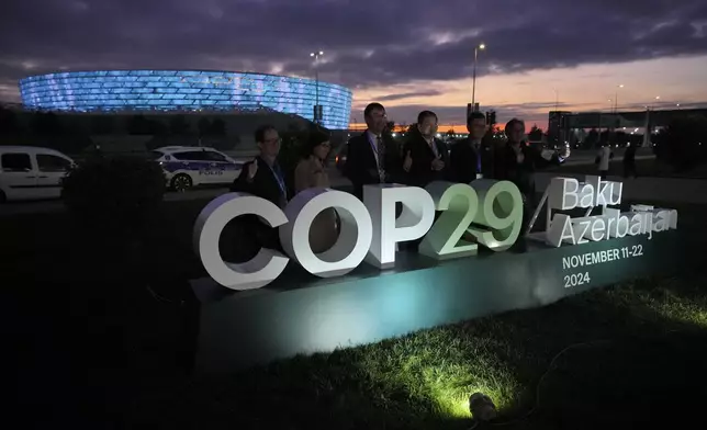 People pose for a photo with the Baku Olympic Stadium in the background at the COP29 U.N. Climate Summit, Thursday, Nov. 14, 2024, in Baku, Azerbaijan. (AP Photo/Peter Dejong)