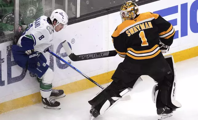 Boston Bruins goaltender Jeremy Swayman (1) raises his stick towards Vancouver Canucks right wing Conor Garland (8) after clearing the puck from behind the net during the first period of an NHL hockey game, Tuesday, Nov. 26, 2024, in Boston. (AP Photo/Charles Krupa)