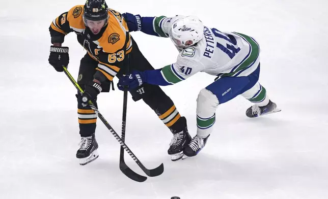 Vancouver Canucks center Elias Pettersson (40) tries to keep Boston Bruins left wing Brad Marchand (63) away from the puck during the first period of an NHL hockey game, Tuesday, Nov. 26, 2024, in Boston. (AP Photo/Charles Krupa)