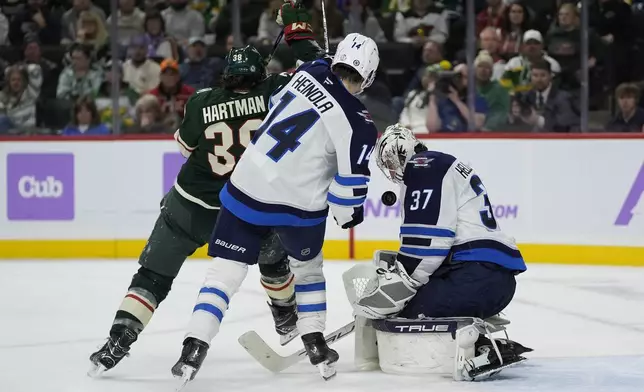 Winnipeg Jets goaltender Connor Hellebuyck (37) and defenseman Ville Heinola (14) defend against Minnesota Wild right wing Ryan Hartman (38) during the third period of an NHL hockey game, Monday, Nov. 25, 2024, in St. Paul, Minn. (AP Photo/Abbie Parr)