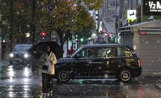 A woman walks along the Oxford Street as snow falls in London, Tuesday, Nov. 19, 2024. (AP Photo/Kin Cheung)