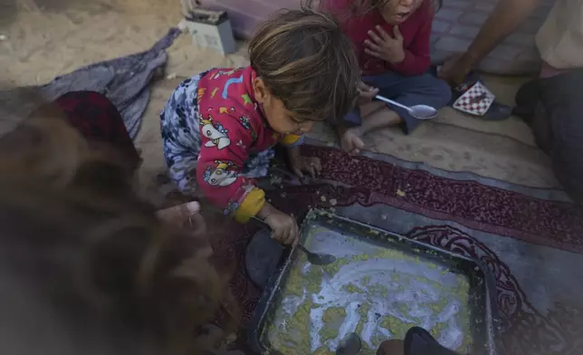 Girls in the Eid family eat lentils cooked by their mother, Yasmin, at their tent in a refugee camp in Deir al-Balah, Gaza Strip, Tuesday Nov. 19, 2024. (AP Photo/Abdel Kareem Hana)