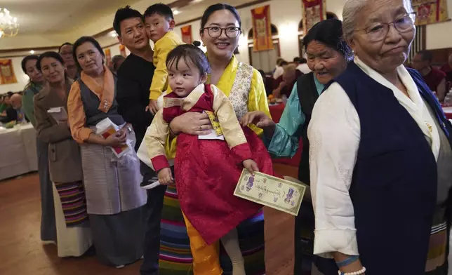 Tenzin Lhasa holds her daughter, Dawoe Tenzin Arya, while in procession to present U.S.-born Buddhist lama, Jalue Dorje, with “khata,” the Tibetan ceremonial scarves that symbolize auspiciousness, at his 18th birthday and enthronement ceremony, in Isanti, Minn., on Saturday, Nov. 9, 2024. (AP Photo/Jessie Wardarski)