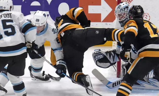 Pittsburgh Penguins' Sidney Crosby, center, is upended in front of Utah Hockey Club goaltender Karel Vejmelka, right rear, and defender Ian Cole (28) during the first period of an NHL hockey game Saturday, Nov. 23, 2024, in Pittsburgh. (AP Photo/Gene J. Puskar)