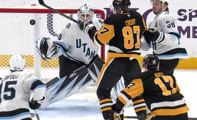 Pittsburgh Penguins' Sidney Crosby (87) attempts to swat the puck out of the air in front of Utah Hockey Club goaltender Karel Vejmelka (70) with Liam O'Brien (38) defending during the first period of an NHL hockey game Saturday, Nov. 23, 2024, in Pittsburgh. (AP Photo/Gene J. Puskar)