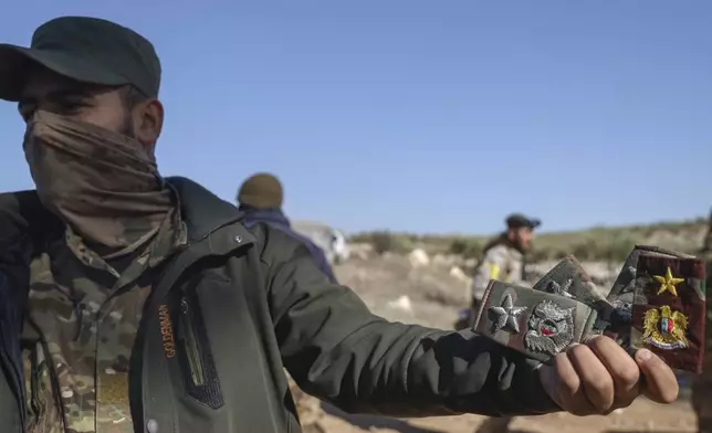 A Syrian opposition fighter displays badges allegedly belonging to Syrian army officers uniforms in Anjara, western outskirts of Aleppo, Syria, Thursday Nov. 28, 2024. (AP Photo/Omar Albam)