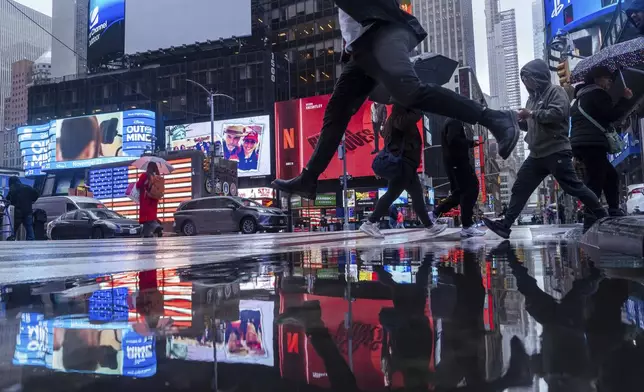 A person jumps over a rain puddle as people cross the street in Times Square, Thursday, Nov. 21, 2024, in New York. (AP Photo/Adam Gray)