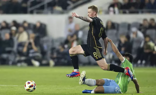 Los Angeles FC midfielder Lewis O'Brien (8) dribbles the ball over the tackle by Seattle Sounders midfielder Obed Vargas (18) during the first half of an MLS Western Conference semifinal soccer match in Los Angeles, Saturday, Nov. 23, 2024. (AP Photo/Kyusung Gong)