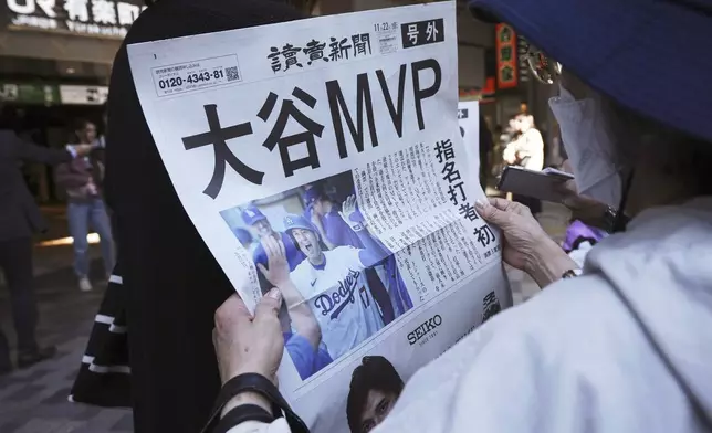 A person reads an extra edition of the Yomiuri Shimbun newspaper reporting that Los Angeles Dodgers' Shohei Ohtani won his third Most Valuable Player award, Friday, Nov. 22, 2024, in Tokyo. (AP Photo/Eugene Hoshiko)