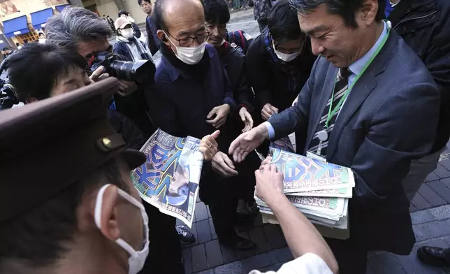 A staff member distributes an extra edition of the Sports Hochi newspaper reporting that Los Angeles Dodgers' Shohei Ohtani won his third Most Valuable Player award, Friday, Nov. 22, 2024, in Tokyo. (AP Photo/Eugene Hoshiko)