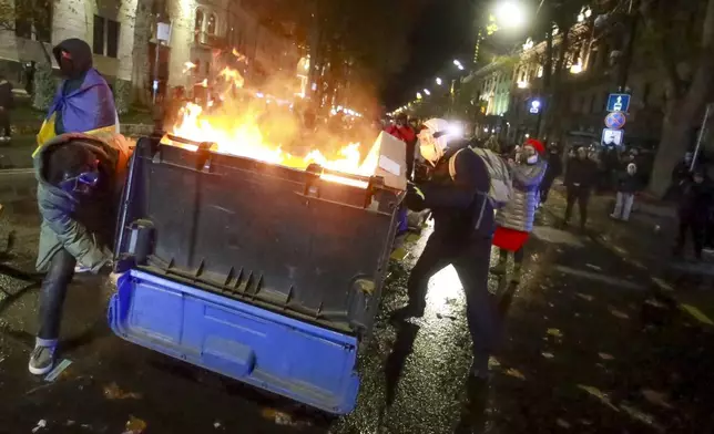 A group of protesters move a burning garbage container pouring into the streets following Georgian Prime Minister Irakli Kobakhidze's announcement, rallying outside the parliament building in Tbilisi, Georgia, on Friday, Nov. 29, 2024. (AP Photo/Zurab Tsertsvadze)