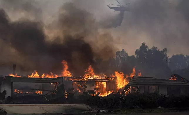 A helicopter drops water over a burning home in the Mountain fire, Wednesday, Nov. 6, 2024, near Camarillo, Calif. (AP Photo/Marcio Jose Sanchez)