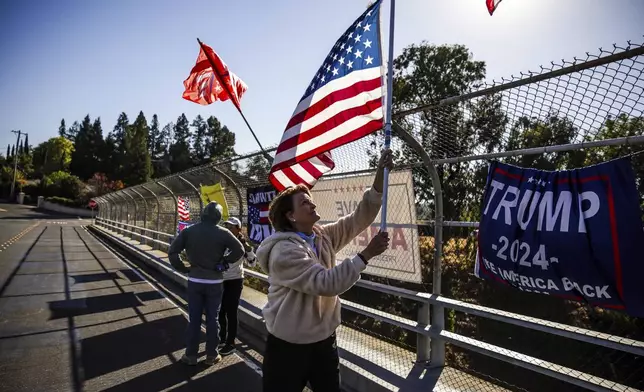 Trump supporter Diana Trouy, center, waves an American flag along the El Curtola Boulevard overpass in Lafayette, Calif., on Wednesday, Nov. 6, 2024. (Gabrielle Lurie/San Francisco Chronicle via AP)