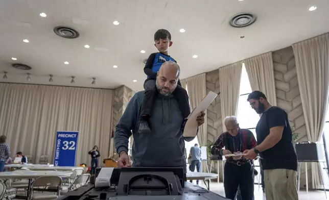 Three-year-old Zayn, sits on his father's shoulders as he inserts his ballot into a machine to vote at the First Presbyterian Church of Dearborn, on Election Day, Tuesday, Nov. 5, 2024, in Dearborn, Mich. (AP Photo/David Goldman)