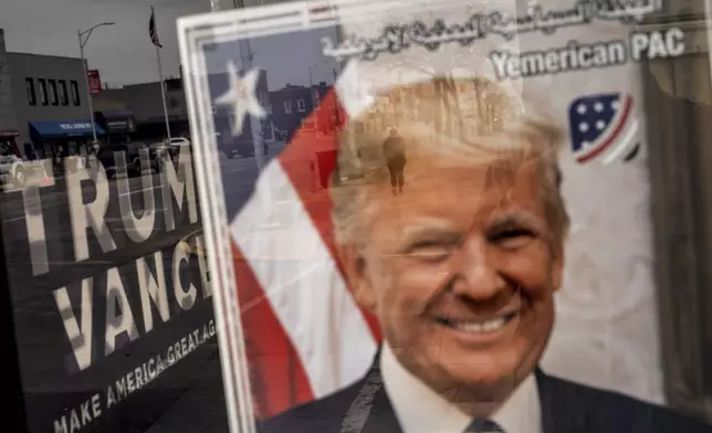 An image of Republican presidential nominee former President Donald Trump hangs in the window of a campaign office as a pedestrian passes by, Monday, Nov. 4, 2024, in Hamtramck, Mich. (AP Photo/David Goldman)