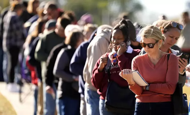 Vanessa Starke, from Lee's Summit, Mo., reads a book about halfway though her 90 minute wait in line to cast her ballot at an early voting location, Thursday, Oct. 31, 2024, in Blue Springs, Mo. (AP Photo/Charlie Riedel)