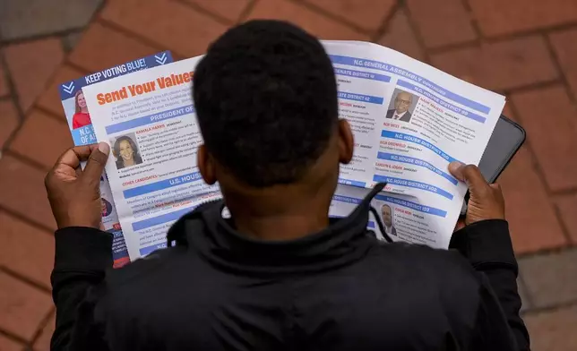 A man reads election materials before voting during the last day of early voting, Saturday, Nov. 2, 2024, in Charlotte, N.C. (AP Photo/Mike Stewart)