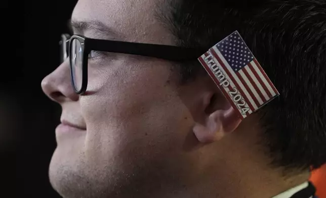 A delegate wearing a small American flag on his ear watches as Republican presidential candidate and former president, Donald Trump, speaks during the final day of the Republican National Convention Thursday, July 18, 2024, in Milwaukee. (AP Photo/Paul Sancya)