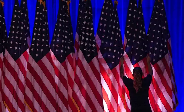 A worker adjusts the flags on stage ahead of an election night watch party for Republican presidential nominee former President Donald Trump Tuesday, Nov. 5, 2024, in West Palm Beach, Fla. (AP Photo/Julia Demaree Nikhinson)