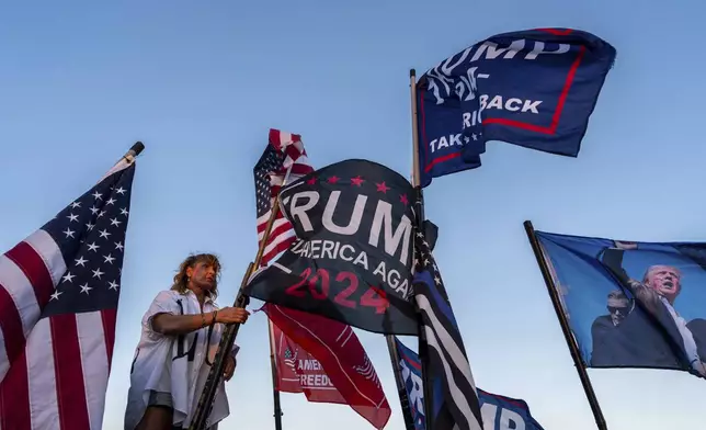 Nikki Fuller, 56, sets up flags on her truck near the Mar-a-Lago estate of President-elect Donald Trump, Monday, Nov. 11, 2024, in Palm Beach, Fla. (AP Photo/Julia Demaree Nikhinson)