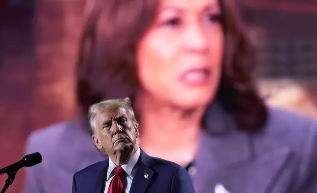 Republican presidential nominee former President Donald Trump watches as a video featuring Democratic presidential nominee Vice President Kamala Harris plays during a campaign event, Friday, Oct. 18, 2024 in Detroit. (AP Photo/Evan Vucci)