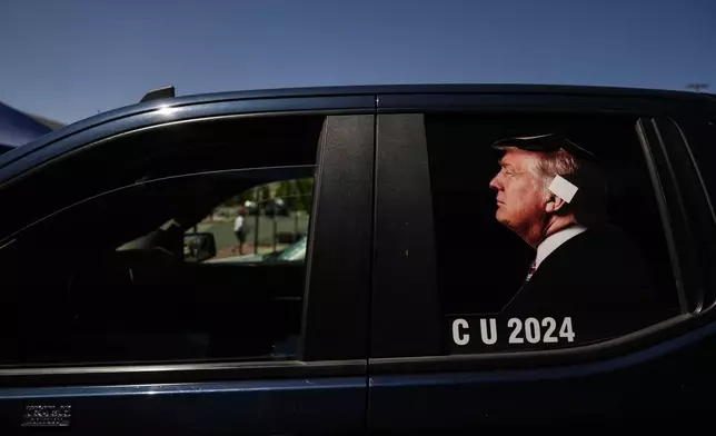 A photo illustrating Republican presidential candidate Donald Trump with an ear bandage is posted on the window of a pickup truck before a campaign event with Republican vice presidential candidate Sen. JD Vance, R-Ohio, in Reno, Nev., Tuesday, July 30, 2024. (AP Photo/Jae C. Hong)