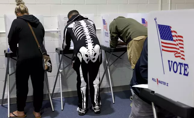 Ready for Halloween, Mark Reynolds, center, votes early beside his wife Jennifer, left, at the St. Charles County Election Authority in St. Charles, Mo. on Thursday, Oct. 31, 2024. (Robert Cohen/St. Louis Post-Dispatch via AP)