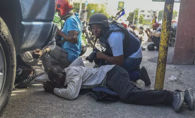 Journalists take cover from the exchange of gunfire between gangs and police in Port-au-Prince, Haiti, Monday, Nov. 11, 2024. (AP Photo/Odelyn Joseph)