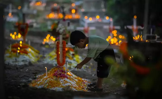 A boy lights a candle at a grave of a deceased relative during All Souls Day, in Guwahati, India, Saturday, Nov. 2, 2024. (AP Photo/Anupam Nath)