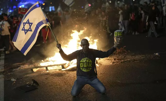 A protester holds an Israeli flag as Israelis light a bonfire during a protest after Prime Minister Benjamin Netanyahu has dismissed his defense minister Yoav Gallant in a surprise announcement in Tel Aviv, Israel, Tuesday, Nov. 5, 2024. (AP Photo/Francisco Seco)