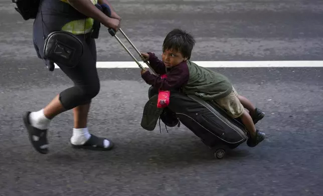 Nayely Nunez, from Honduras, uses her luggage to carry a child as she walks along the highway with a migrant caravan in Huixtla, southern Mexico, heading toward the country's northern border and ultimately the United States, Thursday, Nov. 7, 2024. (AP Photo/Moises Castillo)