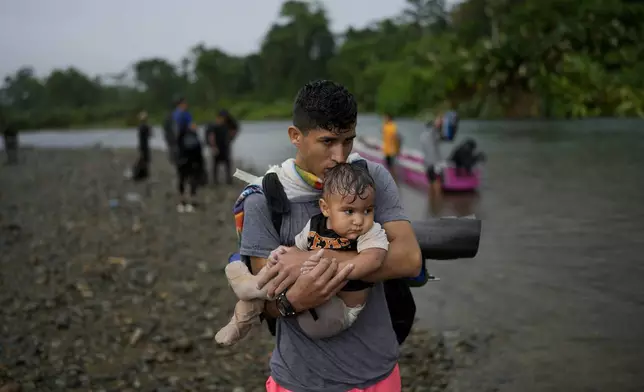 Nelson Pacheco holds the baby of a fellow Venezuelan migrant who are part of a group who walked across the Darien Gap from Colombia as they make their way north to the United States, in Bajo Chiquito, Panama, Friday, Nov. 8, 2024. (AP Photo/Matias Delacroix)