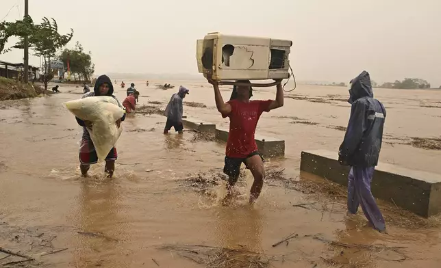 Residents carry their belongings as the river swells, following heavy rains from Typhoon Toraji in Ilagan City, Isabela province, northern Philippines on Monday, Nov. 11, 2024. (AP Photo/Noel Celis)