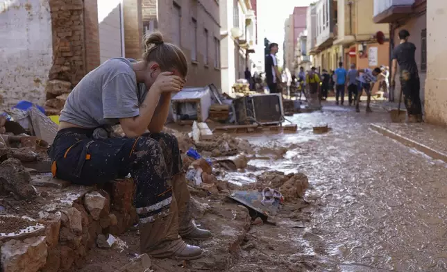 A woman rests as residents and volunteers clean up an area affected by floods in Paiporta, near Valencia, Spain, Friday, Nov. 1, 2024. (AP Photo/Alberto Saiz)