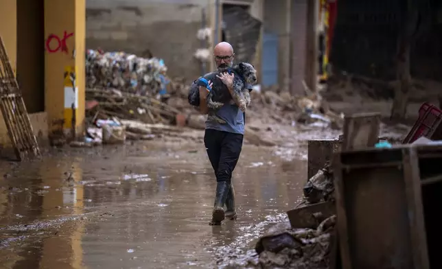 Chimo carries his dog Lou as he walks through the muddy streets after the floods in in Masanasa, Valencia, Spain, Wednesday, Nov. 6, 2024. (AP Photo/Emilio Morenatti)