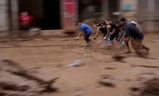 People clear mud from a street in an area affected by floods in Catarroja, Spain, on Monday, Nov. 4, 2024. (AP Photo/Manu Fernandez)