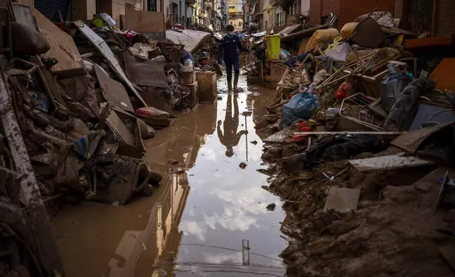 A person walks through a street with piled furniture and rubbish on the sides in an area affected by floods in Paiporta, Valencia, Spain, Tuesday, Nov. 5, 2024. (AP Photo/Emilio Morenatti)