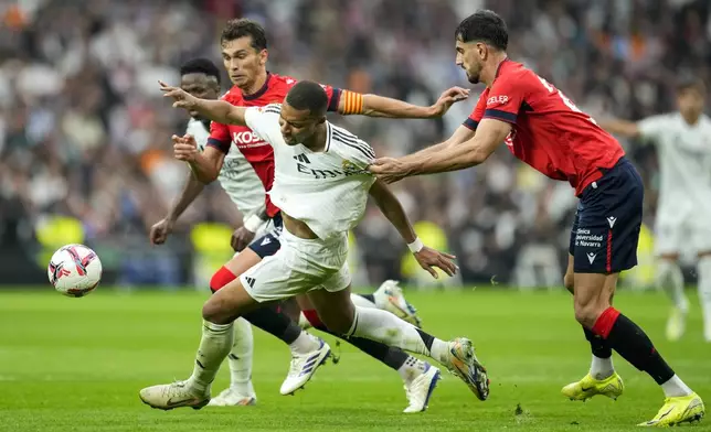 Real Madrid's Kylian Mbappe is challenged by Osasuna's Alejandro Catena, right, during the Spanish La Liga soccer match between Real Madrid and Osasuna at the Santiago Bernabeu stadium in Madrid, Spain, Saturday, Nov. 9, 2024. (AP Photo/Jose Breton)