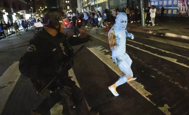 A person covered in blue paint runs from a police officer as fans celebrate on streets after the Los Angeles Dodgers won against the New York Yankees in the baseball World Series Wednesday, Oct. 30, 2024, in Los Angeles. (AP Photo/Ethan Swope)